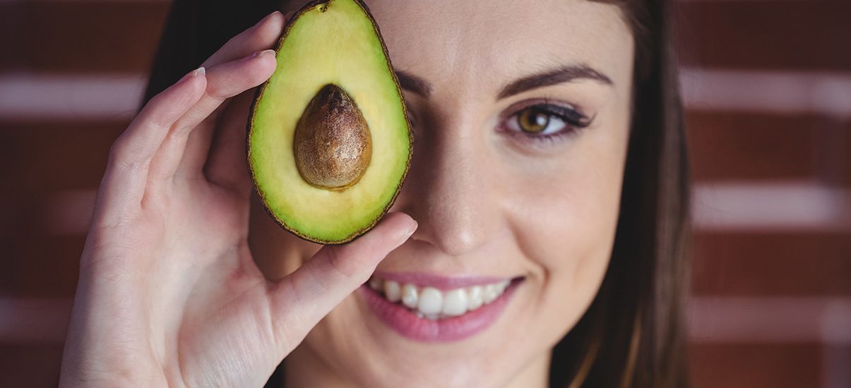 Eine Frau hält sich eine Avocado vor's Auge