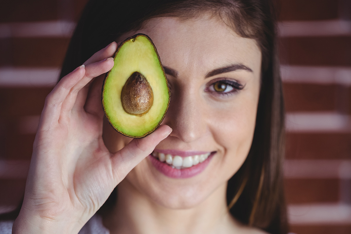Eine Frau hält sich eine Avocado vor's Auge