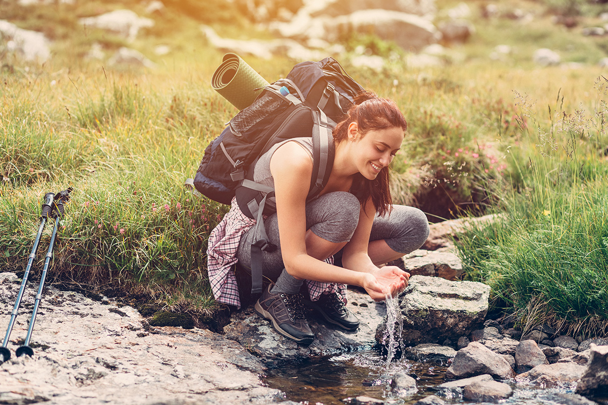 Frau trinkt Wasser aus einem Bergbach