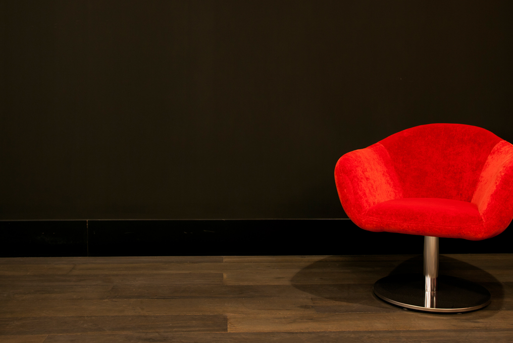 Ein roter Designsessel vor einer dunklen Wand.