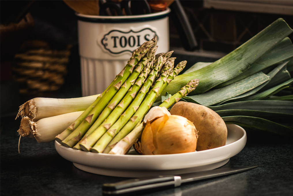 Un piatto con asparagi crudi, cipolla, cipolle, cipolline e patate.