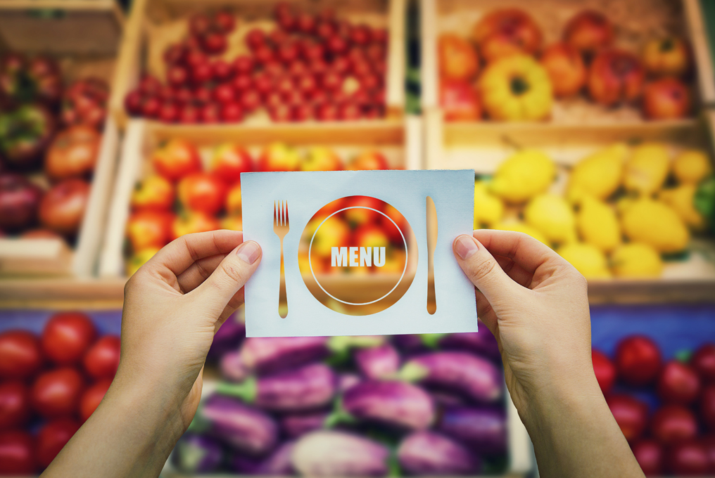 Jemand hält ein Blatt auf dem das Wort Menu mit einer Gabel und einem Messer dargestellt ist.