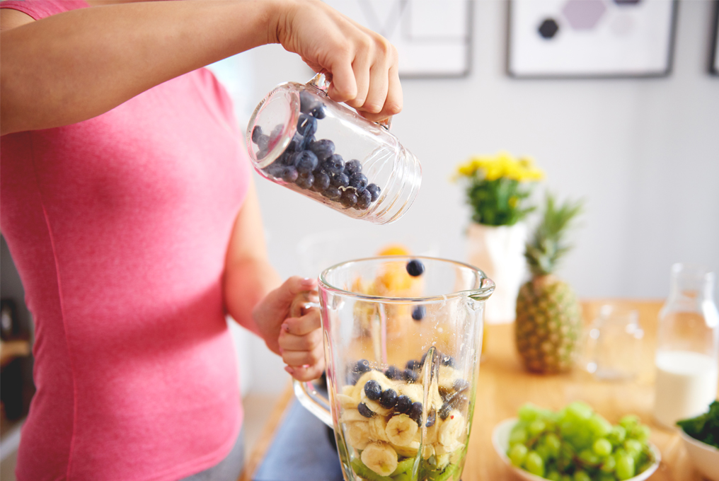Eine Frau tut verschiedene Früchte in den Mixer rein