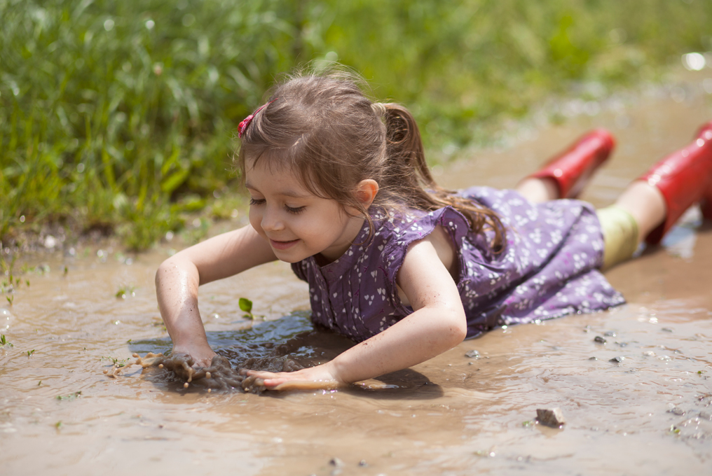 Bambina sdraiata con la pancia nel fango