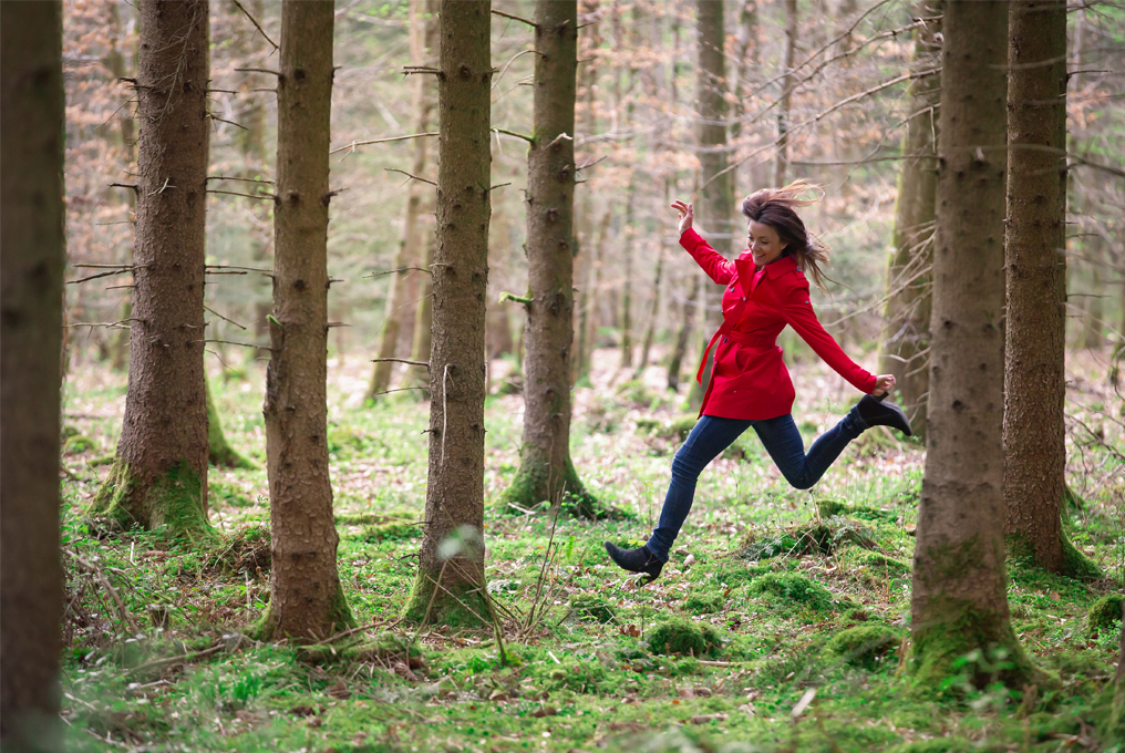 Eine Frau, in einer roten Jacke springt in einem Wald