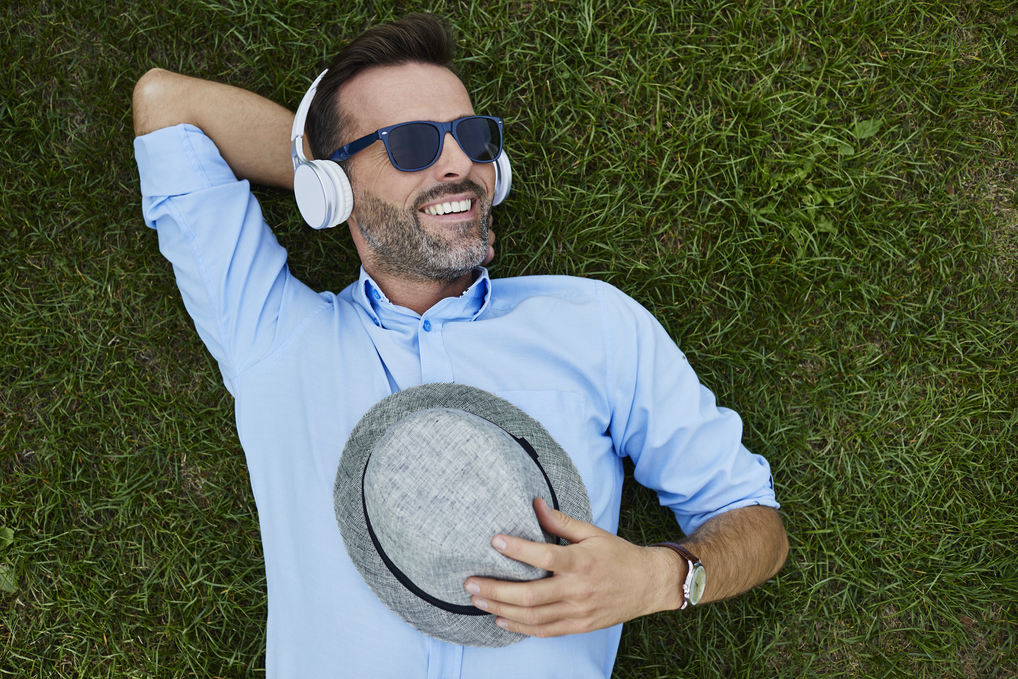 Mann liegt auf einer Wiese mit Sonnenbrille und Kopfhörer