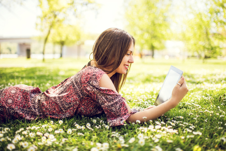 Frau liegt auf einer Wiese und liest ein E-Book
